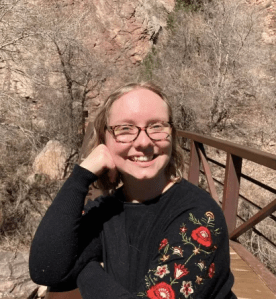 A picture of a young woman in a black sweater with red flowers smiling at the camera.